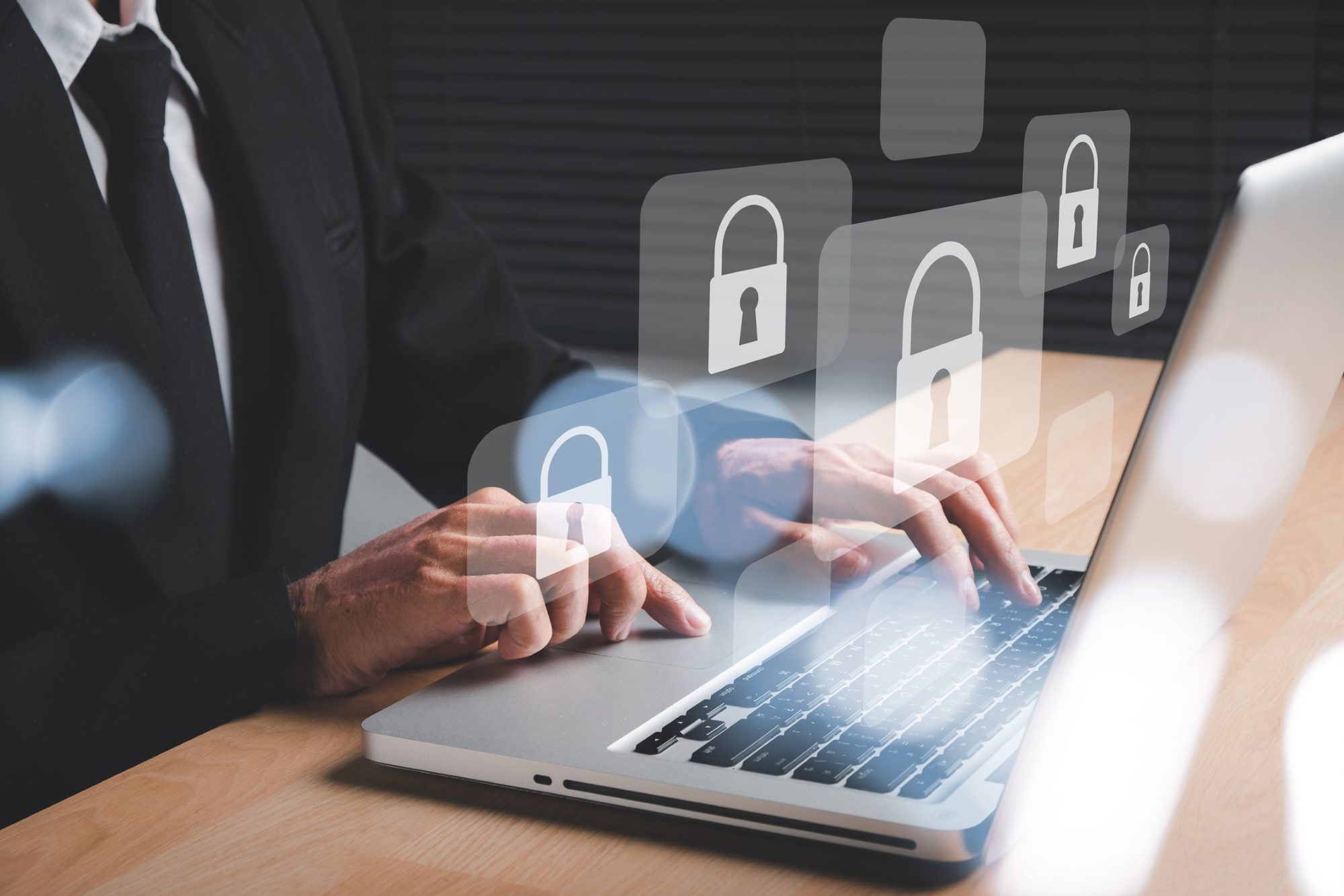 A person in a business suit rests their hands on a laptop computer keyboard while virtual padlock images float in the foreground.