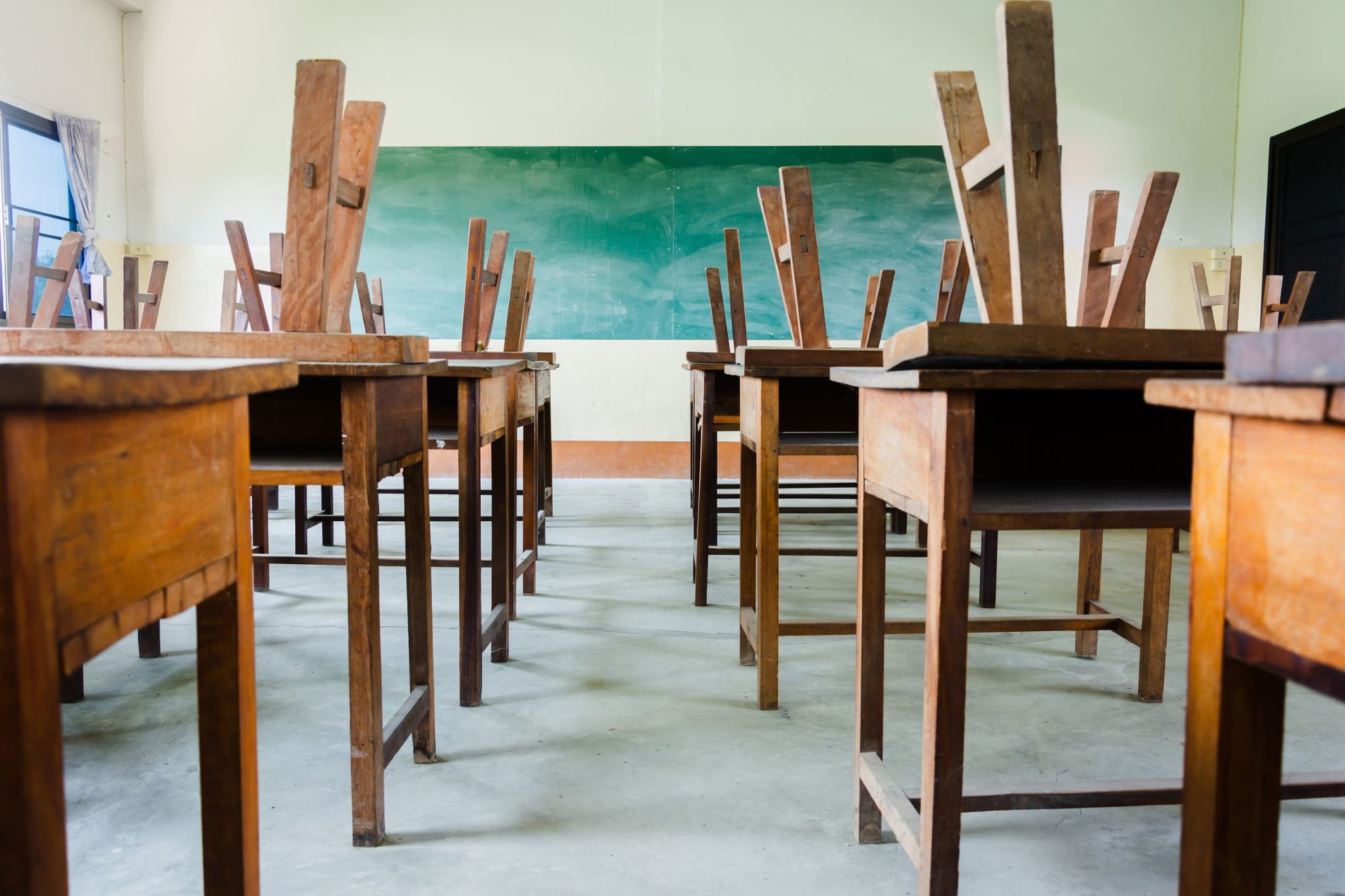 View from the back of a classroom looking past unoccupied desks with chairs stacked on top