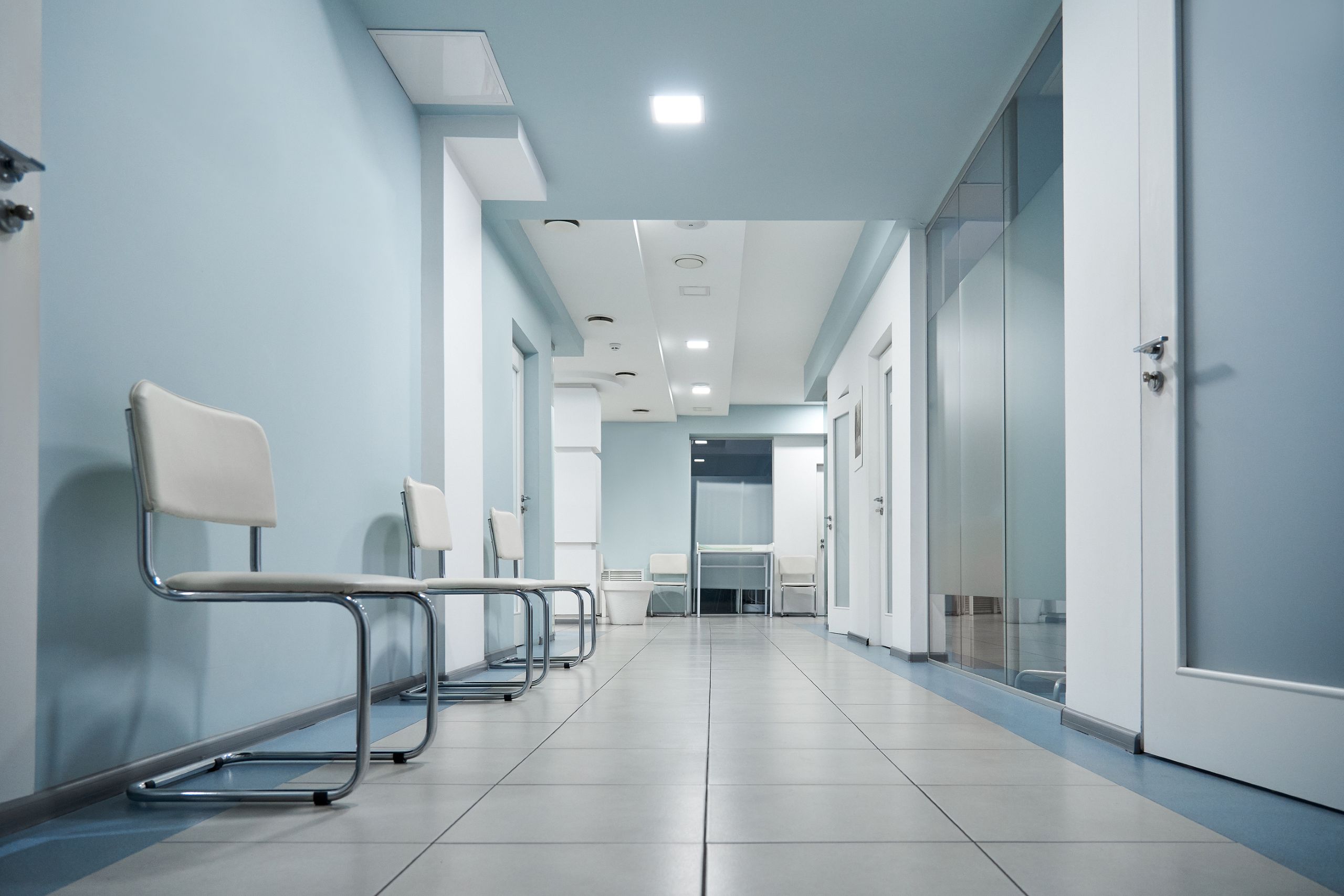 A row of empty chairs sit in a deserted hallway in a medical facility.